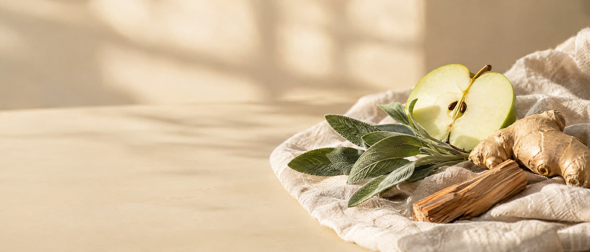 Manzana verde, salvia, jengibre y sándalo sobre lino natural, con luz de mañana entrando por una ventana